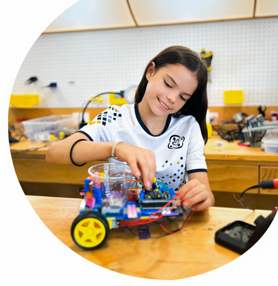 Una niña sonriente, con cabello oscuro, está trabajando en un proyecto de robótica en un laboratorio de Docet.